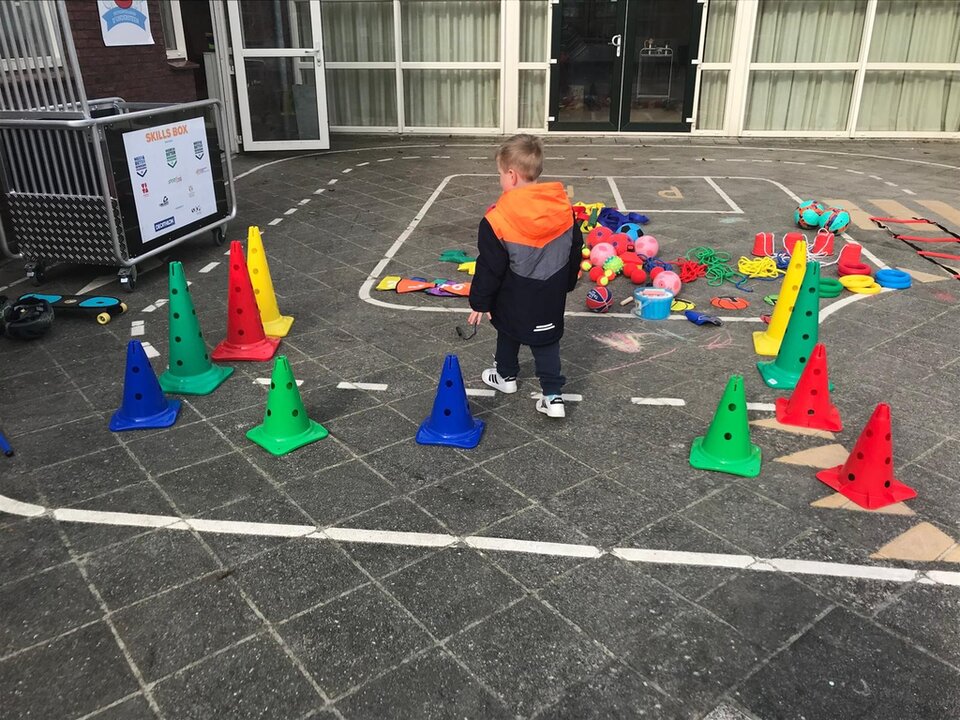 Een jongen loopt over een parcours met pionnen op een schoolplein.