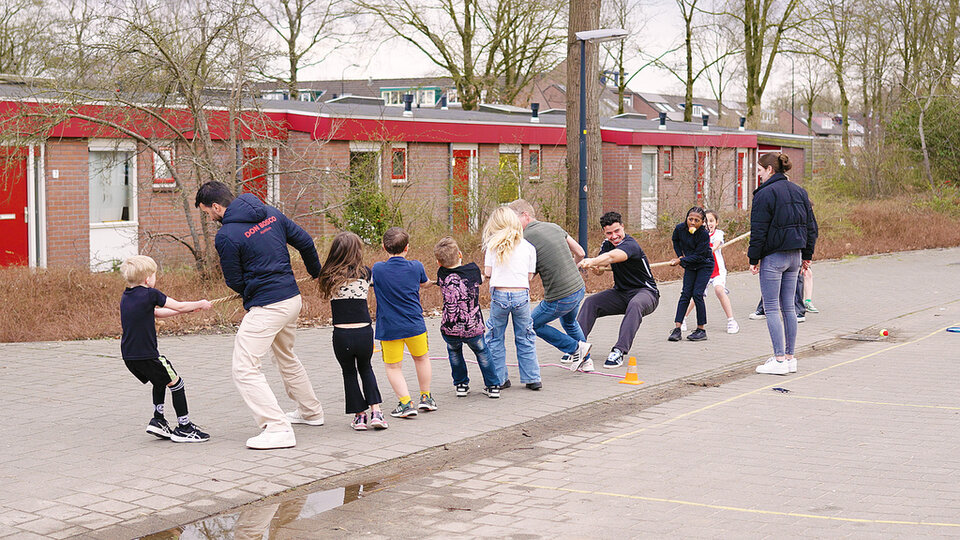 Kinderen en een paar volwassenen doen een potje touwtrekken op straat.